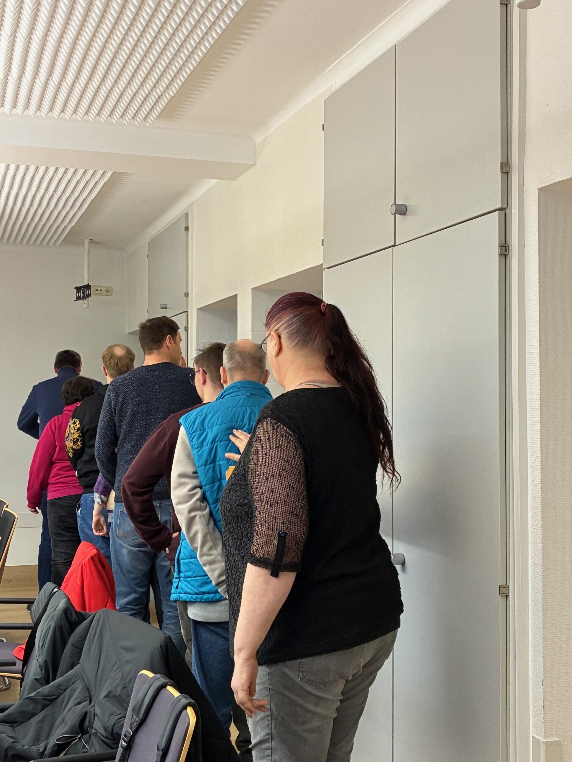 Teilnehmende am Workshop Kommunikationstraining stehen bei einer Übung in einer Reihe hintereinander mit einer Hand auf dem Rücken der nächsten Person